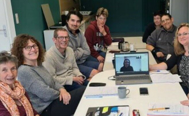 Autour d'une table, les membres du comités sont assis, souriants. Aline est en fond de l'écran de l'ordinateur (travail en distanciel)